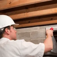 Termite inspection technician checking a basement wall and framing for termite activity in Mobile, AL